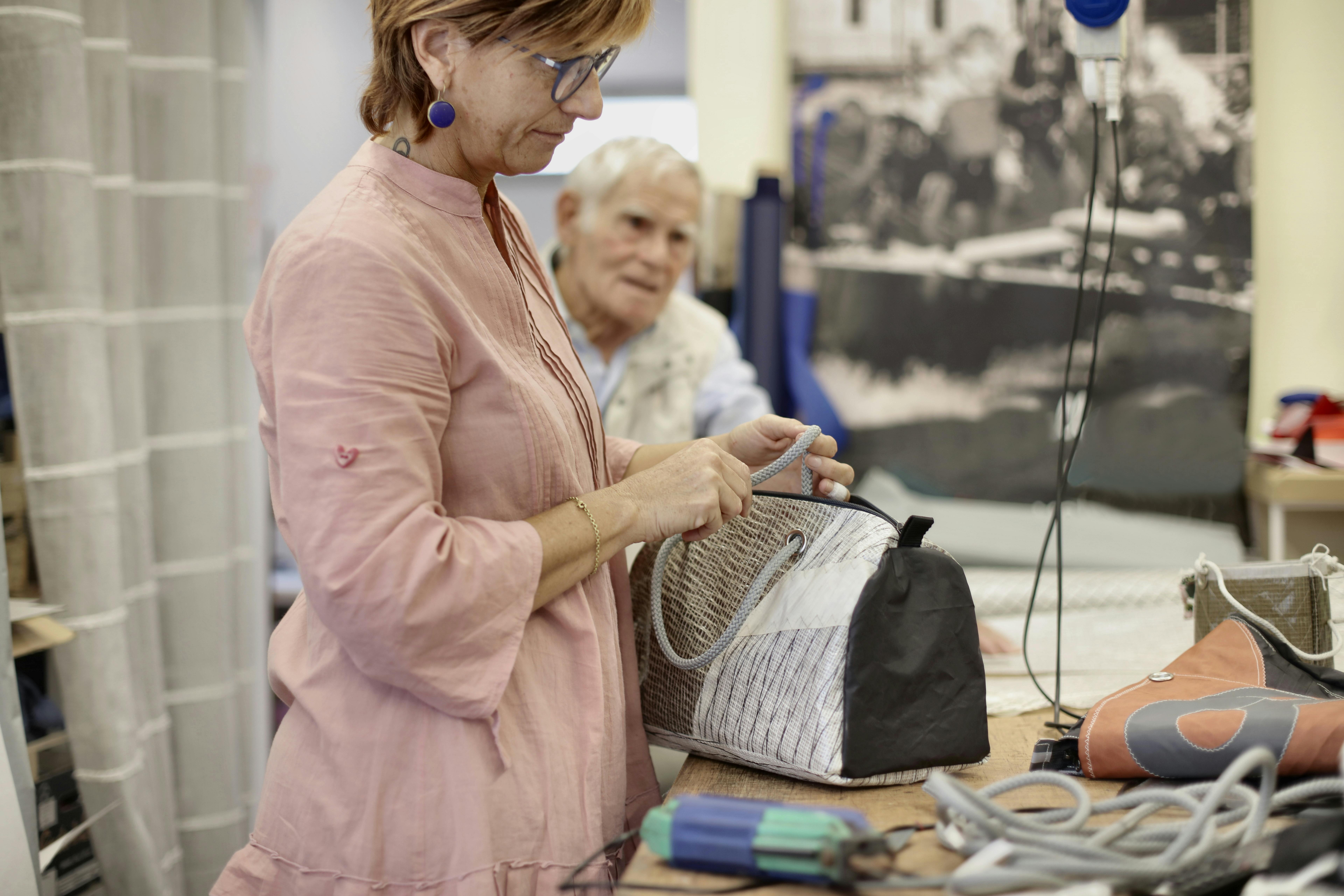 female dressmaker in glasses mending bag for senior client in workshop