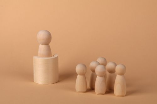 Free Minimalist wooden peg figures arranged against a muted background, depicting leadership concept. Stock Photo