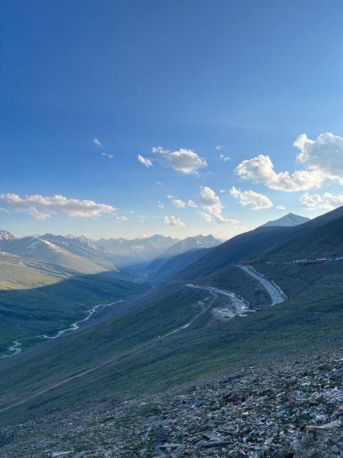 Free Panoramic view of a mountain valley with winding road under a bright blue sky. Stock Photo