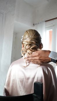 A stylist adjusts a bridal updo hairstyle in a well-lit room.