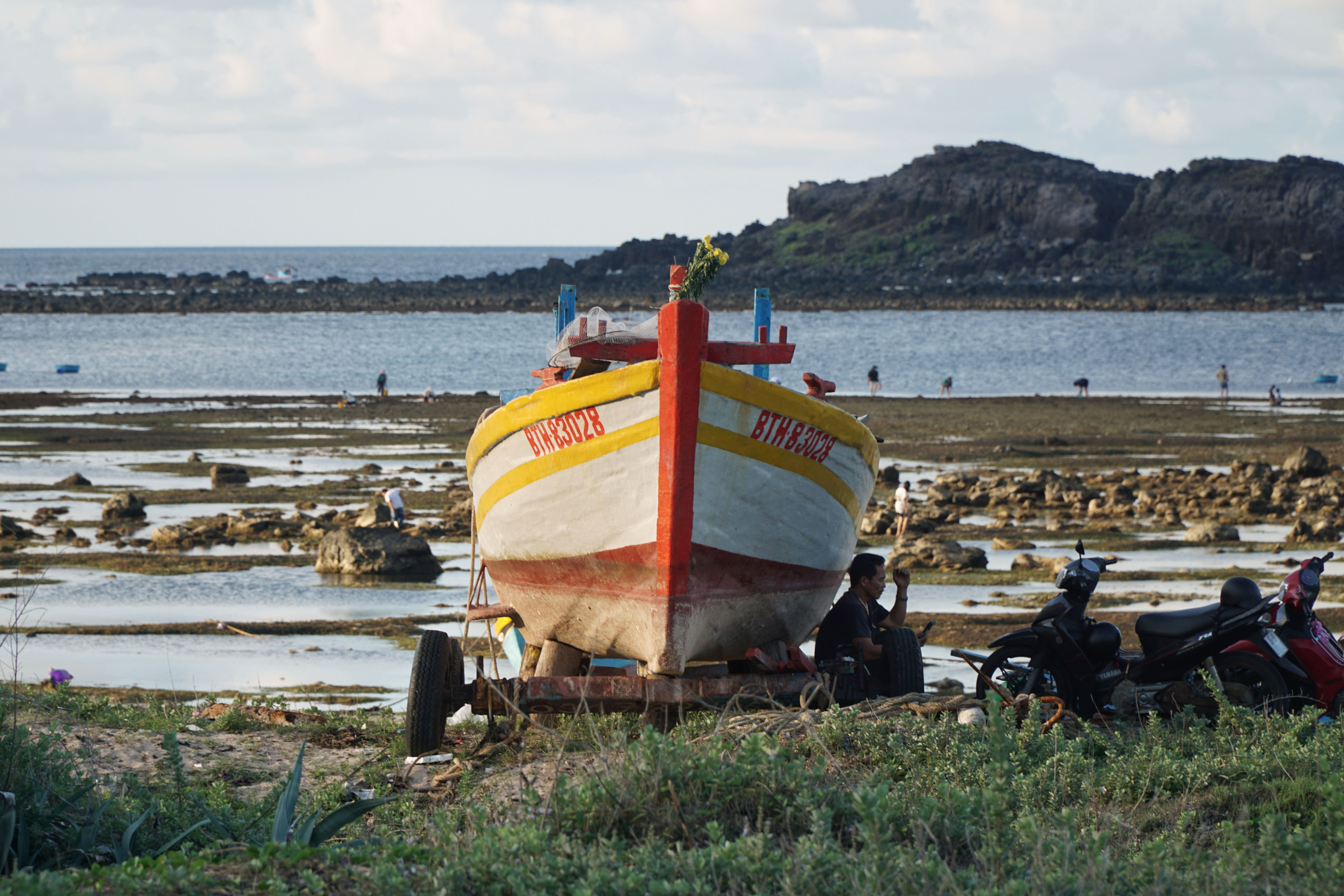 A vibrant fishing boat on the rocky shores of Phu Quy, Vietnam during daylight.
