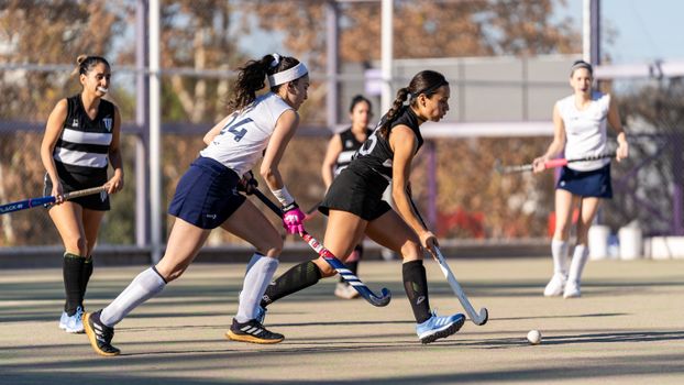 Dynamic action shot capturing female athletes competing in a high-energy field hockey game.