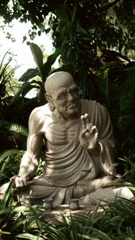 Serene stone statue of a Buddhist monk amid lush greenery in a peaceful garden setting.