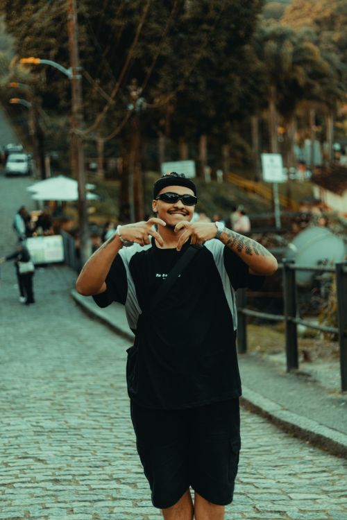 Free Smiling man in sunglasses poses on a cobblestone street with trees in the background. Stock Photo