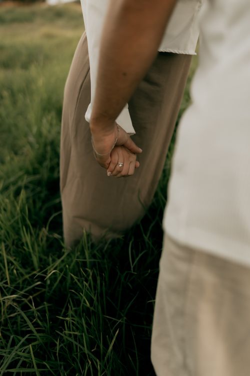 Free Close-up of two people holding hands in a grassy field, symbolizing love and connection. Stock Photo