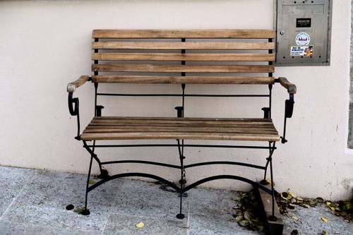 Free A rustic wooden bench sits against a wall in Estavayer-le-Lac, Switzerland, adorned with fallen leaves. Stock Photo