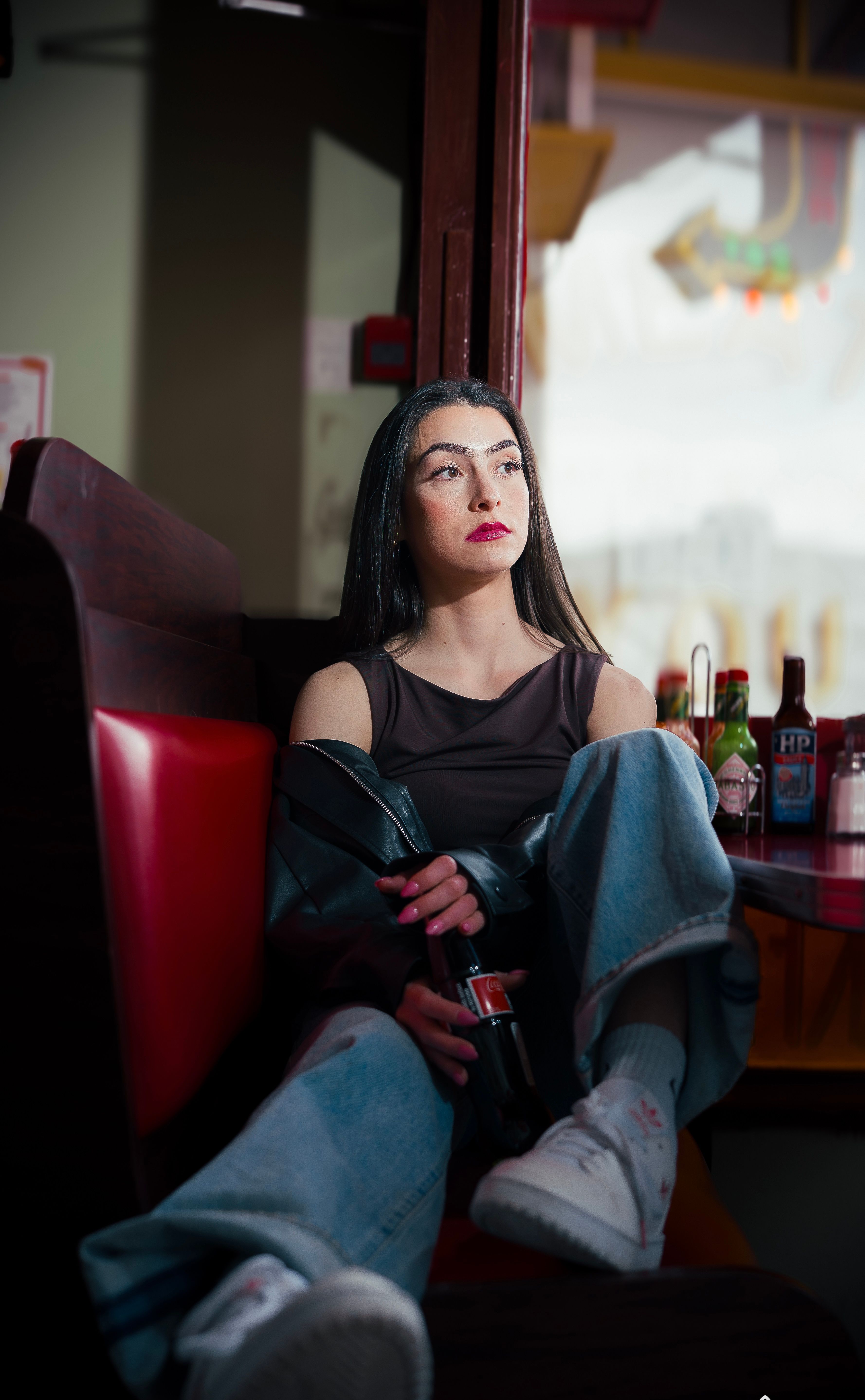 Young woman relaxing in a diner booth in Calgary, Canada, holding a drink, with city view.