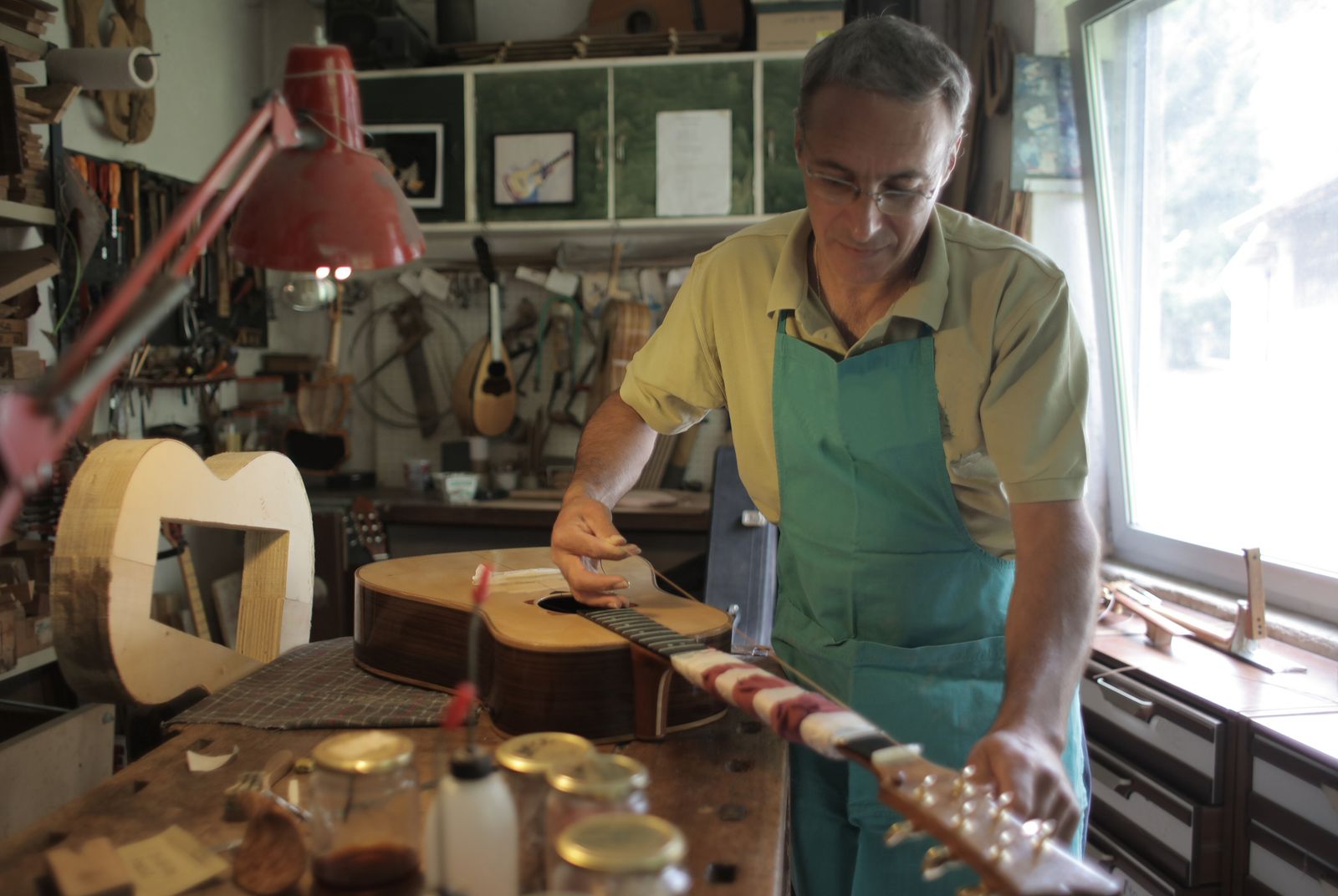 Un artesano con mandil verde trabaja en una guitarra sobre la mesa de su taller
