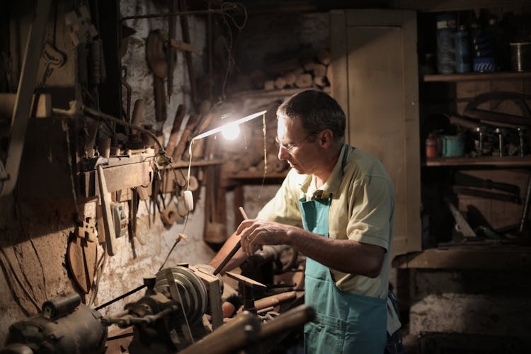 Senior Man Sharpening Metal Detail In Workshop