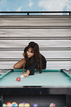 Young woman aiming at billiards table with concentration in an urban setting.