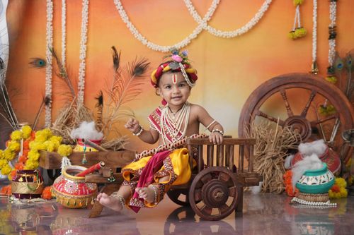 Free Charming baby dressed as Lord Krishna with decorative props, perfect for festive and cultural themes. Stock Photo