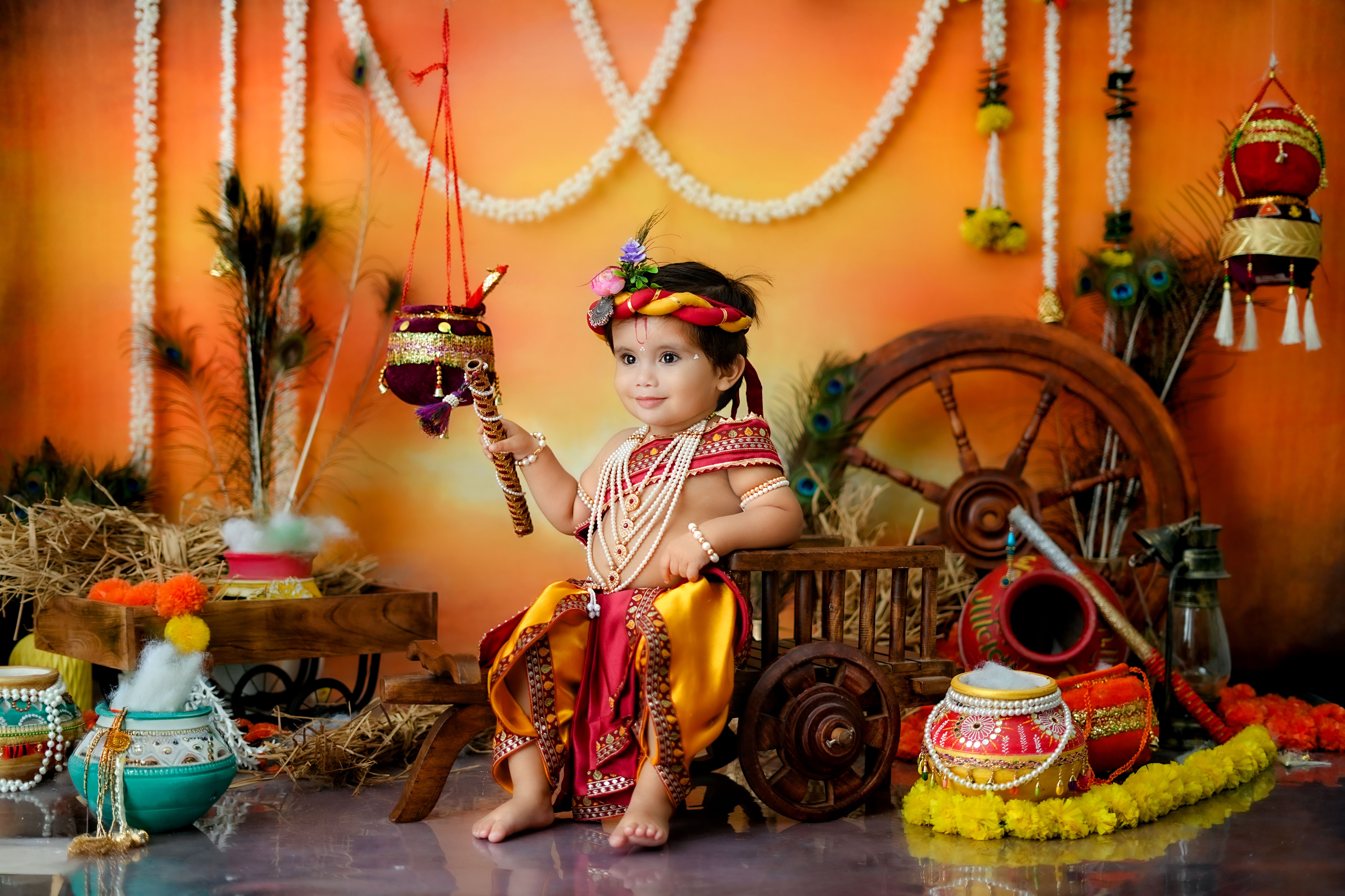 Cute child in Indian attire celebrating Janmashtami with festive decor and colorful props.