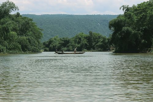 Free Serene river landscape featuring a boat with two people amidst lush green surroundings and hills. Stock Photo