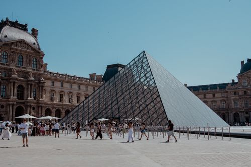 Free Visitors at the iconic Louvre Pyramid in Paris, enjoying a sunny day outside the famous museum. Stock Photo