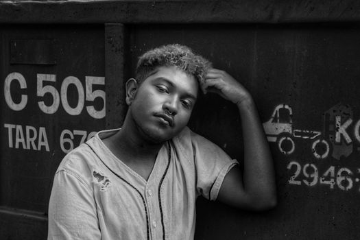 Black and white unhappy thoughtful ethnic male in worn out shirt leaning on metal container and touching forehead while looking at camera with sadness
