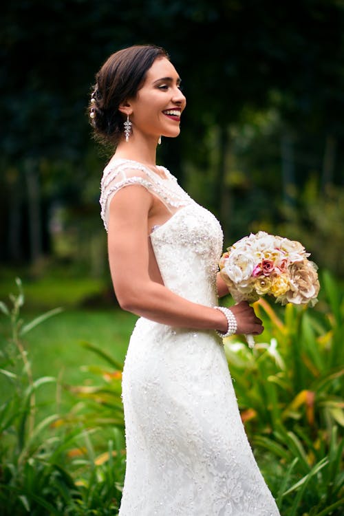 Женщина в белом цветочном свадебном платье с букетом цветов улыбается