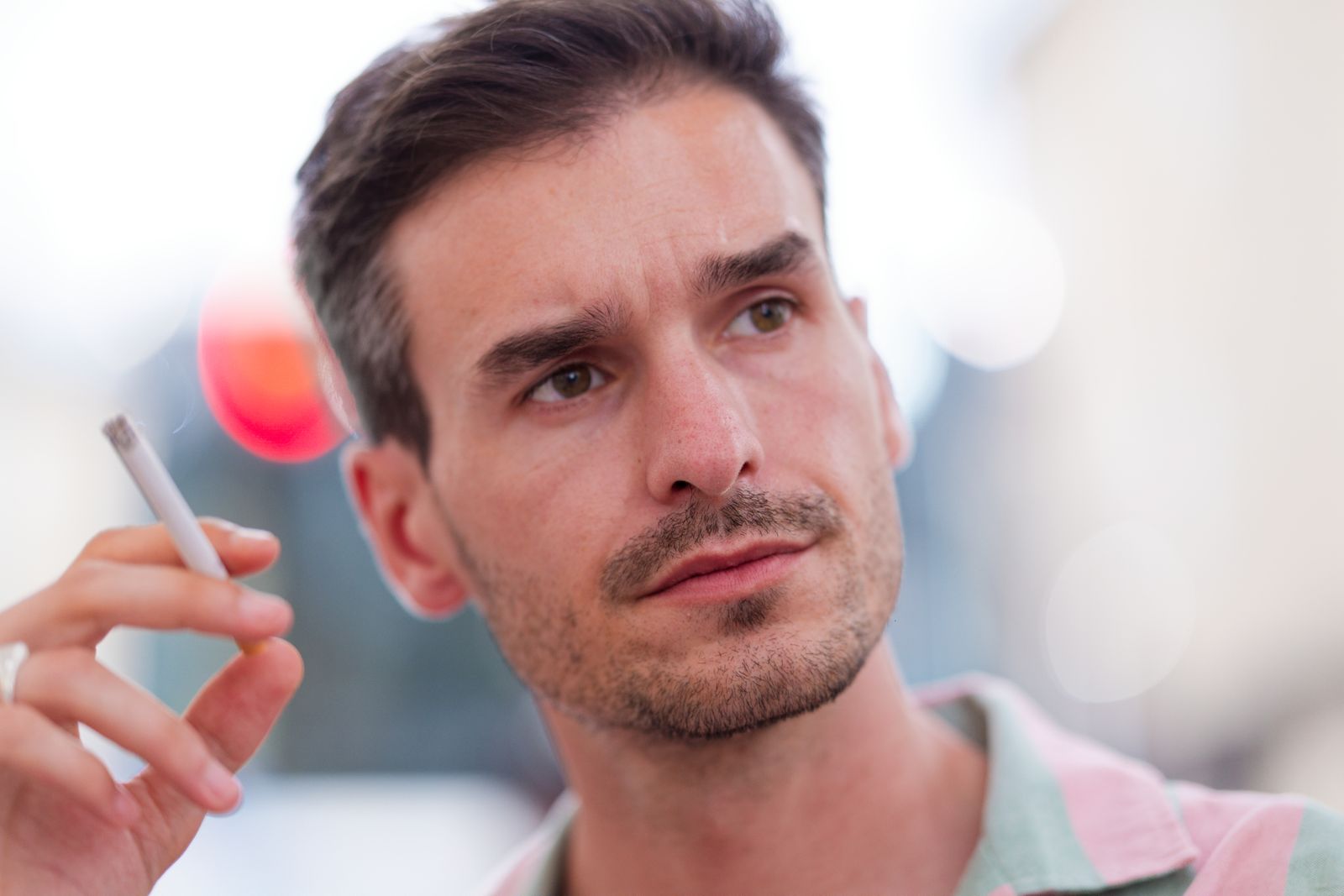 Portrait songeur d'un homme fumant une cigarette, lumières floues en arrière-plan