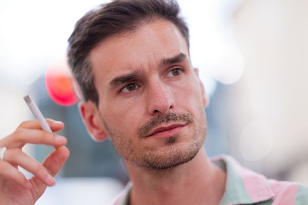 Portrait songeur d'un homme fumant une cigarette, lumières floues en arrière-plan
