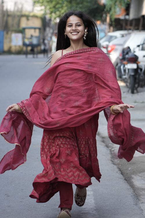 Free Smiling woman in red traditional dress joyfully running on a street on a sunny day, exuding happiness and freedom. Stock Photo