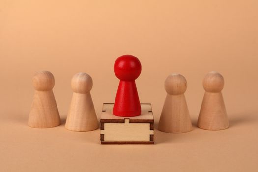 A red pawn stands out as a leader among wooden pieces on a peach background.