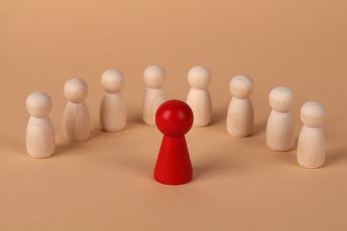 Free Central red wooden figure surrounded by beige figures symbolizing leadership and individuality. Stock Photo