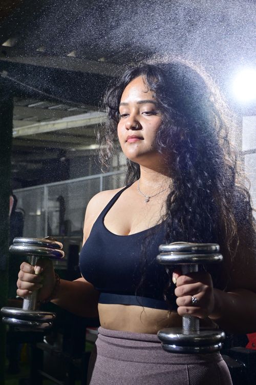 Free Young woman lifting dumbbells indoors with ambient light, capturing strength and focus. Stock Photo