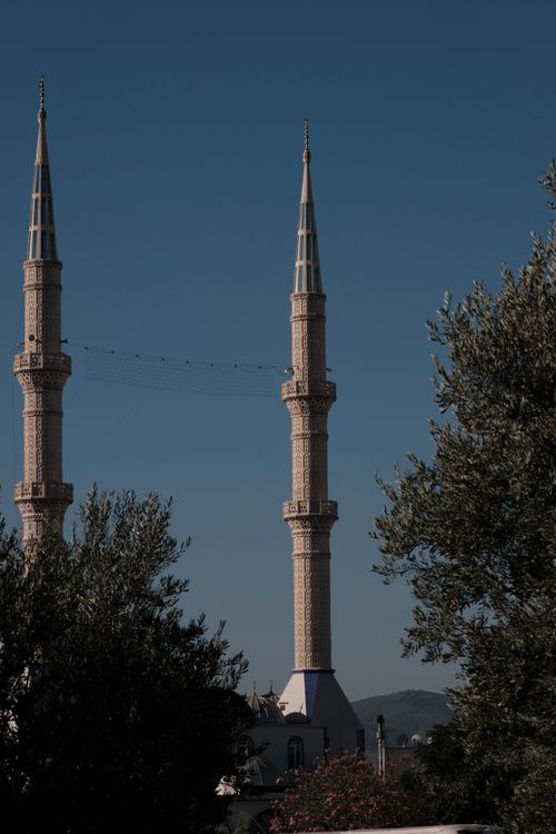 Free Two mosque minarets rise gracefully against a clear blue sky, framed by lush green trees. Stock Photo