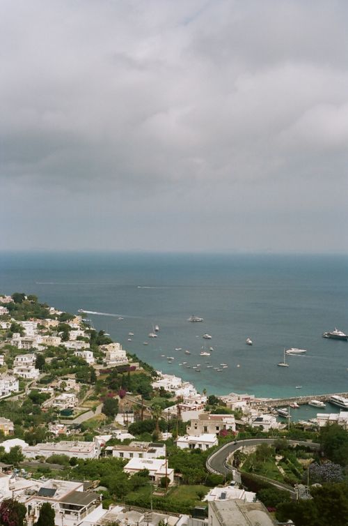 Free A scenic view of Capri's coastline with boats and lush greenery under a cloudy sky. Stock Photo