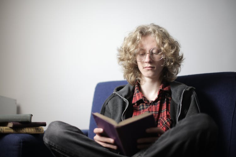 Focused Teen Boy Reading Book On Couch