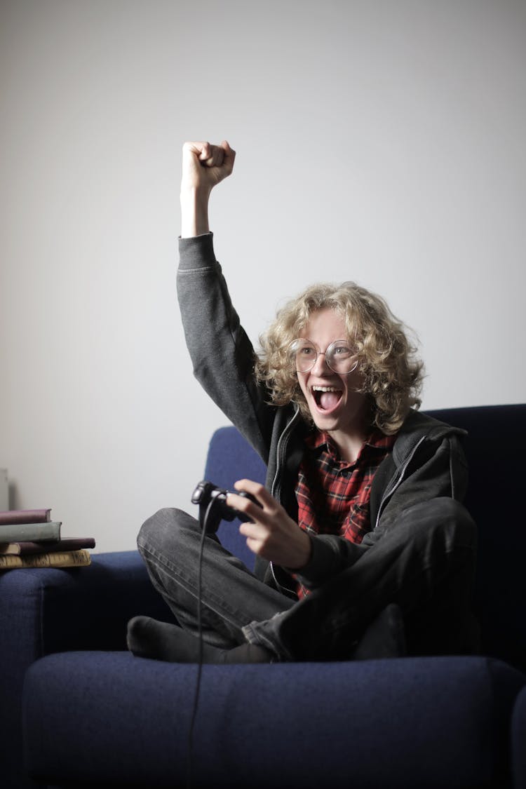 Cheerful Male Teen Playing Video Game On Couch