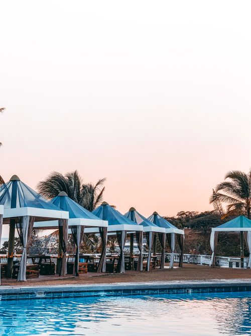 Free Picturesque scenery of swimming pool surrounded with cozy blue umbrellas and comfy deckchairs among tropical palms during scenic sunset Stock Photo