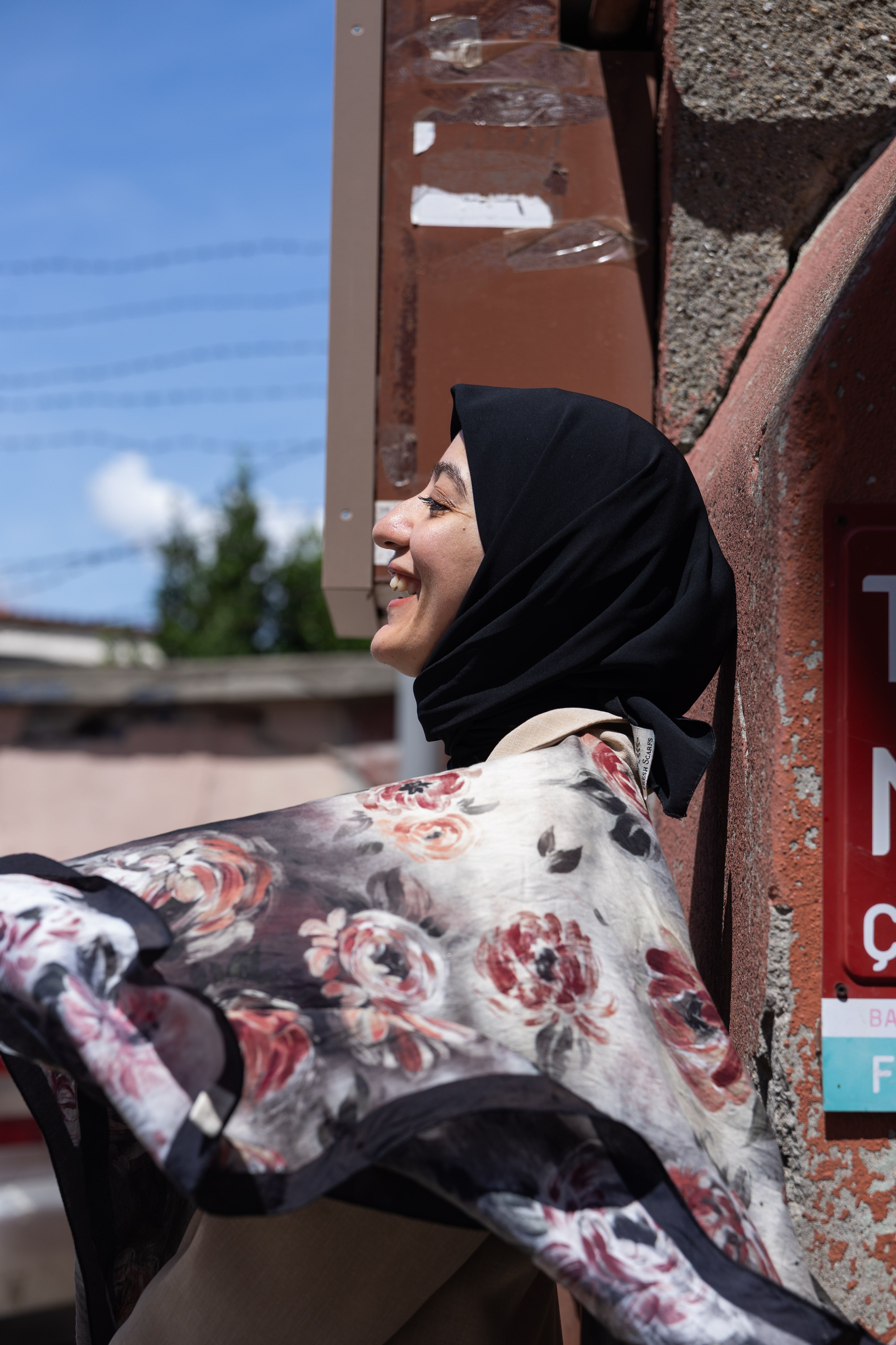 Smiling woman in a headscarf enjoying a sunny day outdoors with a floral scarf.