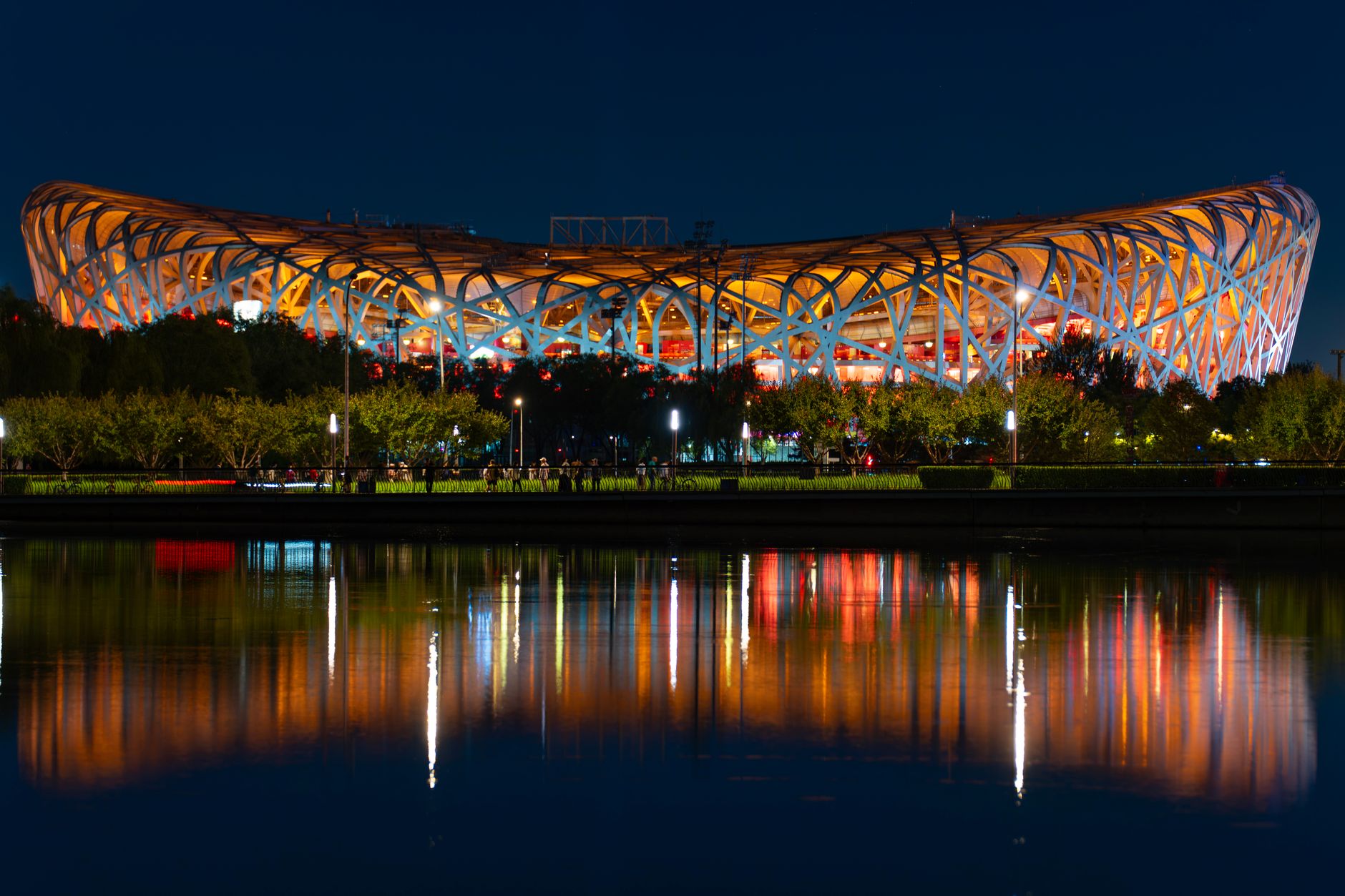 Vibrant nighttime view of Beijing National Stadium with colorful reflections on water.