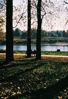 Tranquil autumn scene with people enjoying a river view on a sunny day.