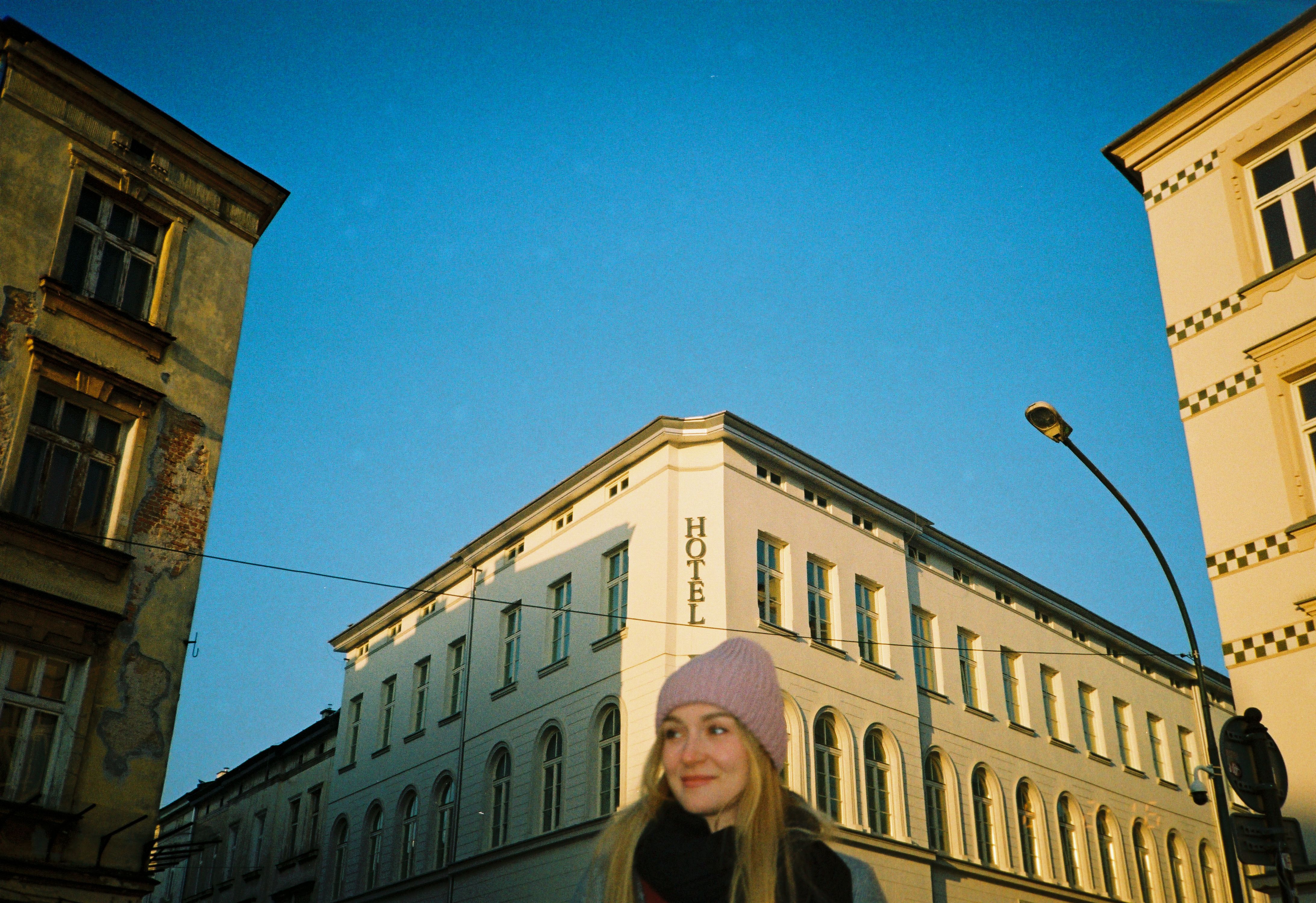 A young woman smiles on a sunny urban street surrounded by historic buildings.