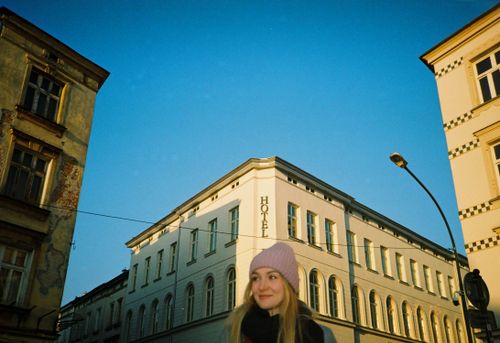 Free A young woman smiles on a sunny urban street surrounded by historic buildings. Stock Photo