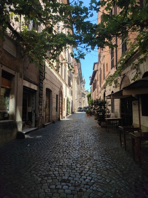Free Sunny cobblestone street lined with historic buildings and greenery in Lazio, Italy. Stock Photo