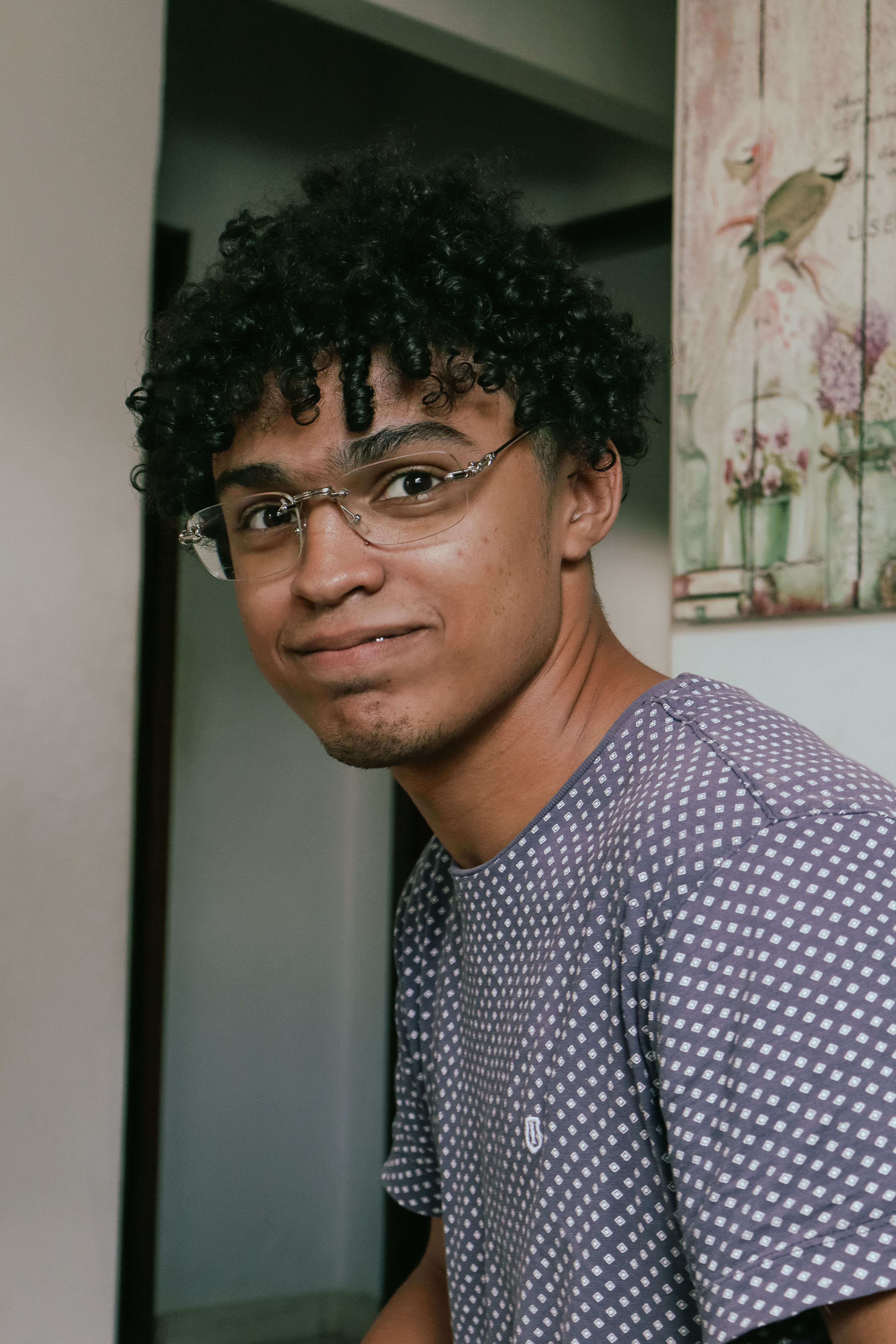 Young man with curly hair and glasses in a casual indoor setting.