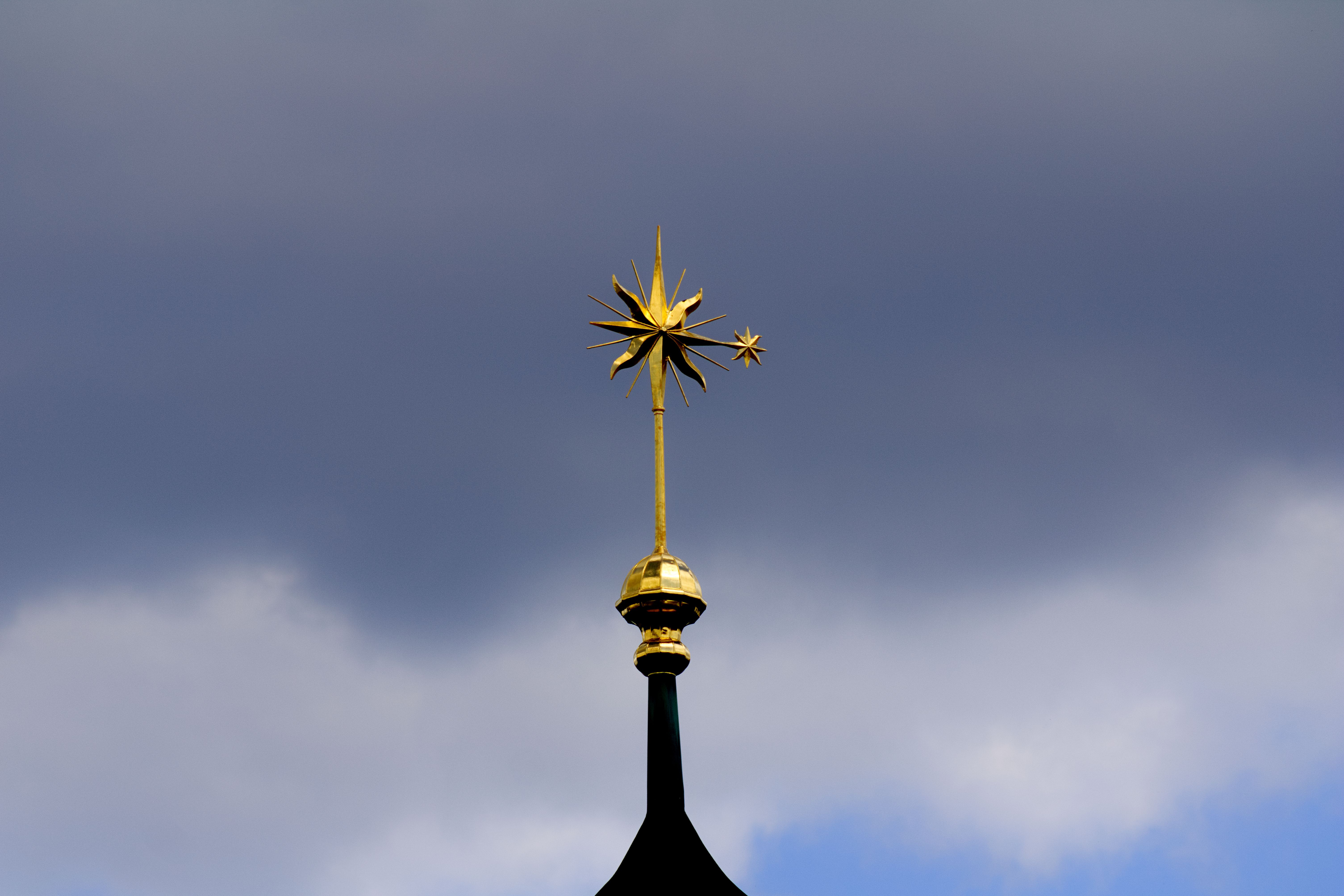A golden spire on a church's steeple set against a dramatic cloudy sky in Germany.
