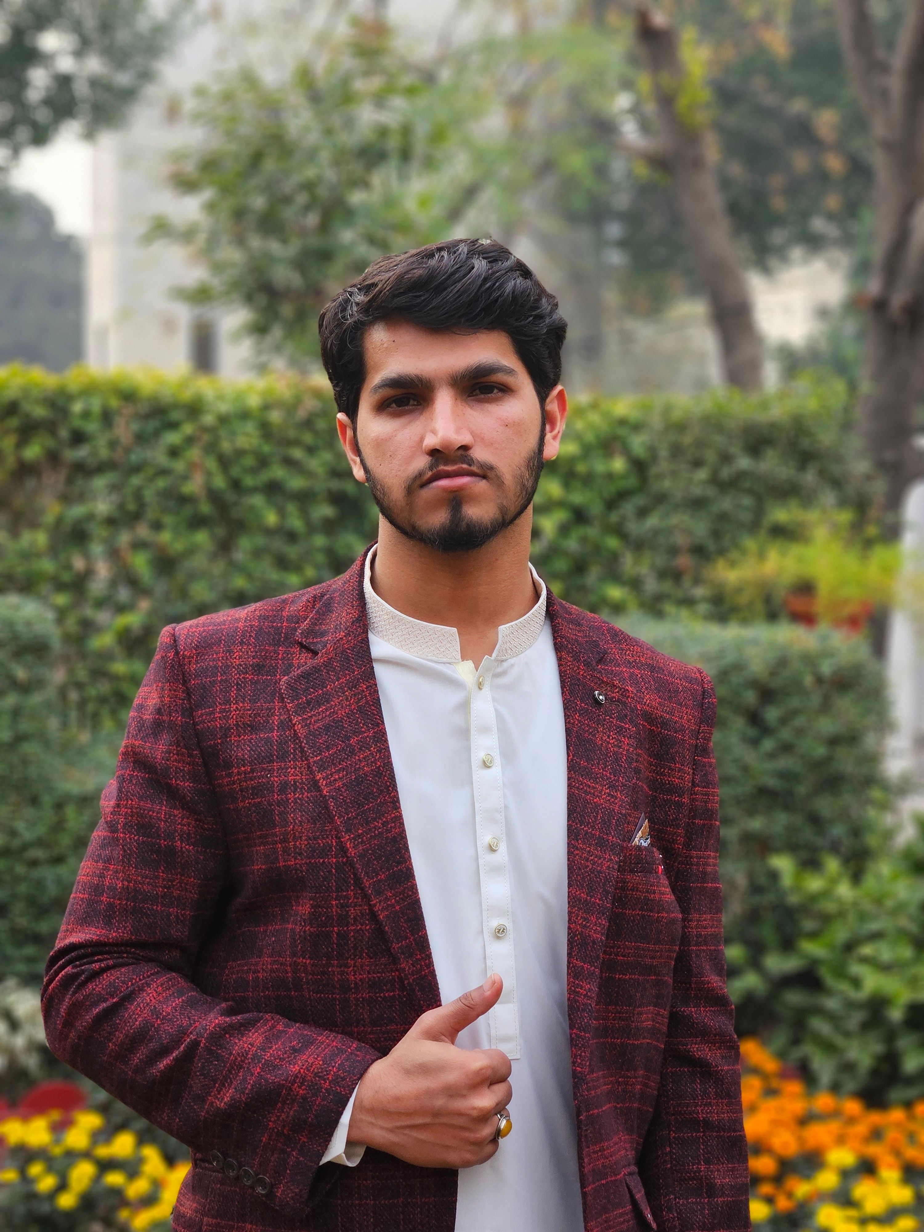 Confident young man in a red plaid suit posing outdoors in a garden setting.
