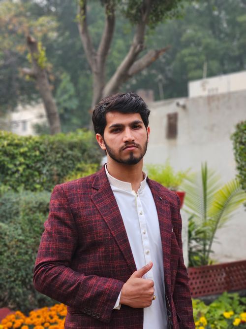 Free Confident young man in a red blazer poses outdoors in a garden setting, showcasing style and fashion. Stock Photo