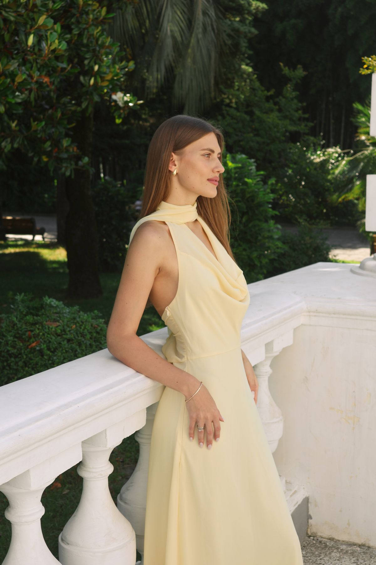 Woman in a pale butter yellow sleeveless midi dress on a sunny balustrade terrace for a daytime wedding