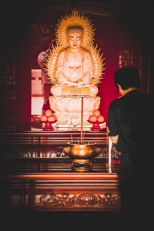 Free A serene image of a worshipper facing a golden Buddhist statue in a temple. Captures a moment of devotion. Stock Photo