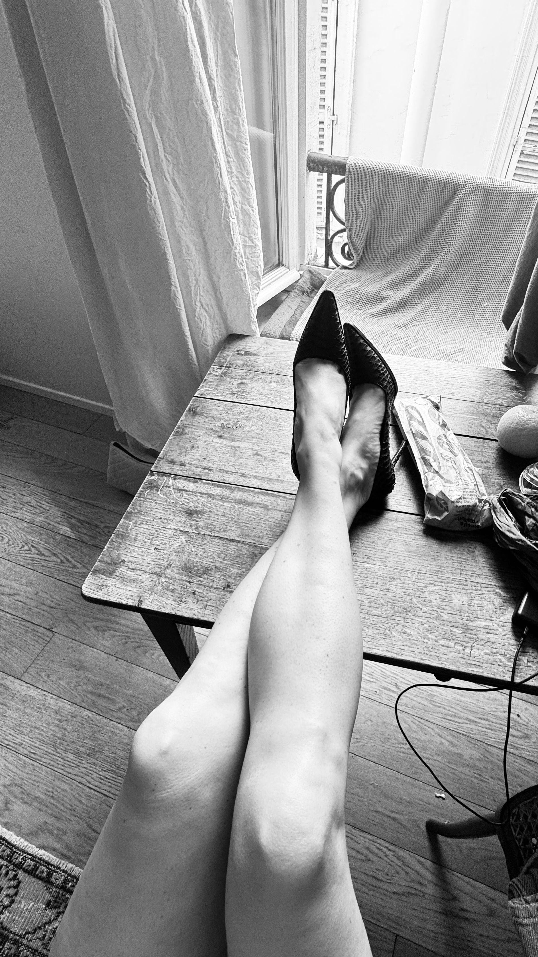 Black and white image of crossed legs on a rustic table, capturing a chic Parisian vibe.
