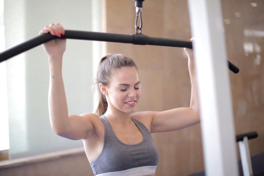 Happy athletic female in sportswear doing exercise using nautilus equipment while training arm muscles and looking down in light modern gym