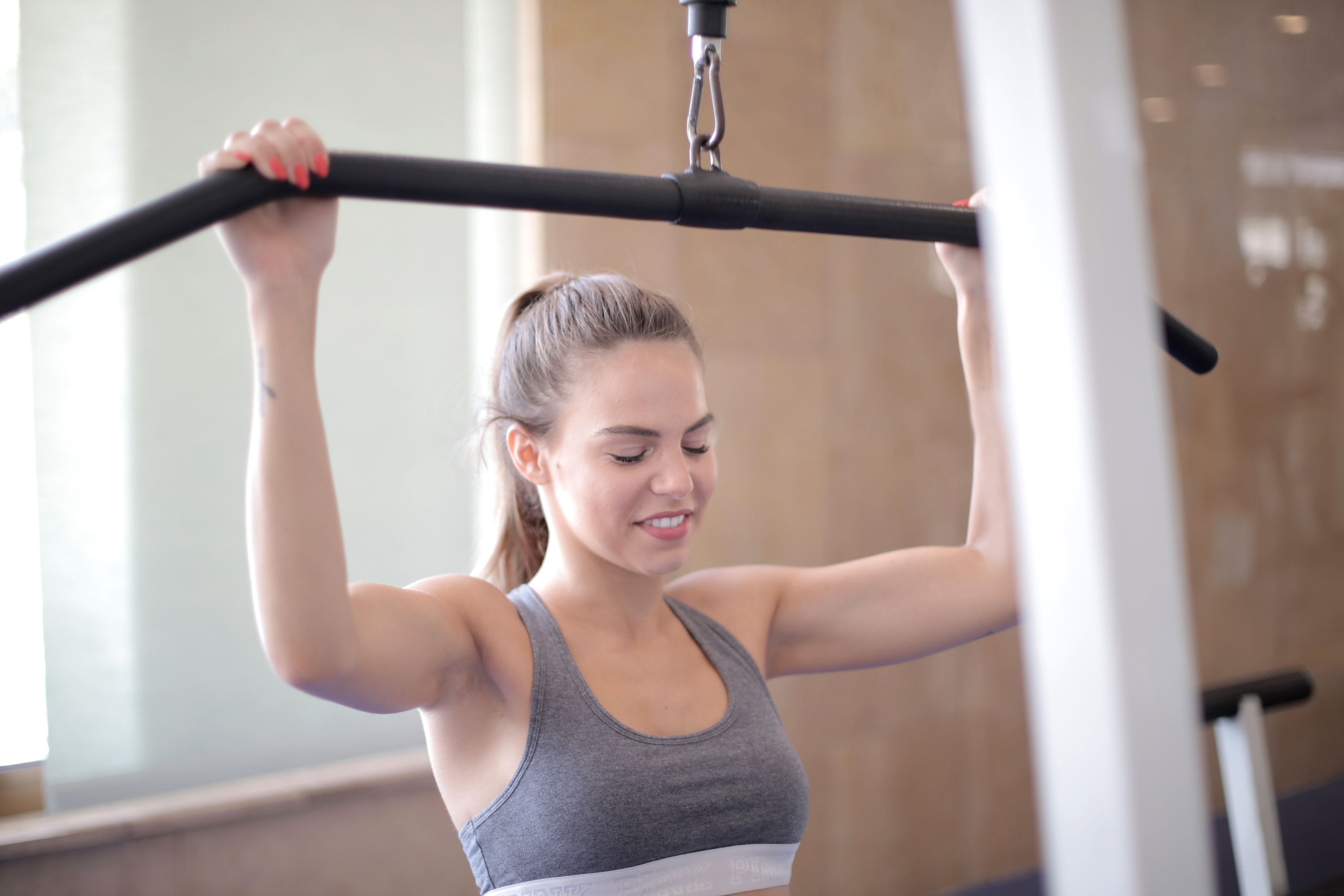 Happy athletic female in sportswear doing exercise using nautilus equipment while training arm muscles and looking down in light modern gym