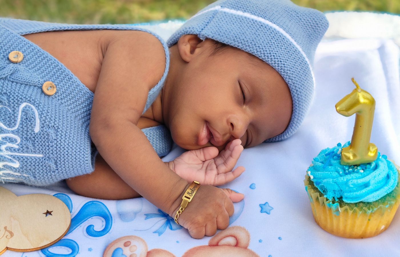 A cute baby sleeping beside a cupcake with a candle shaped like the number one, celebrating first birthday.
