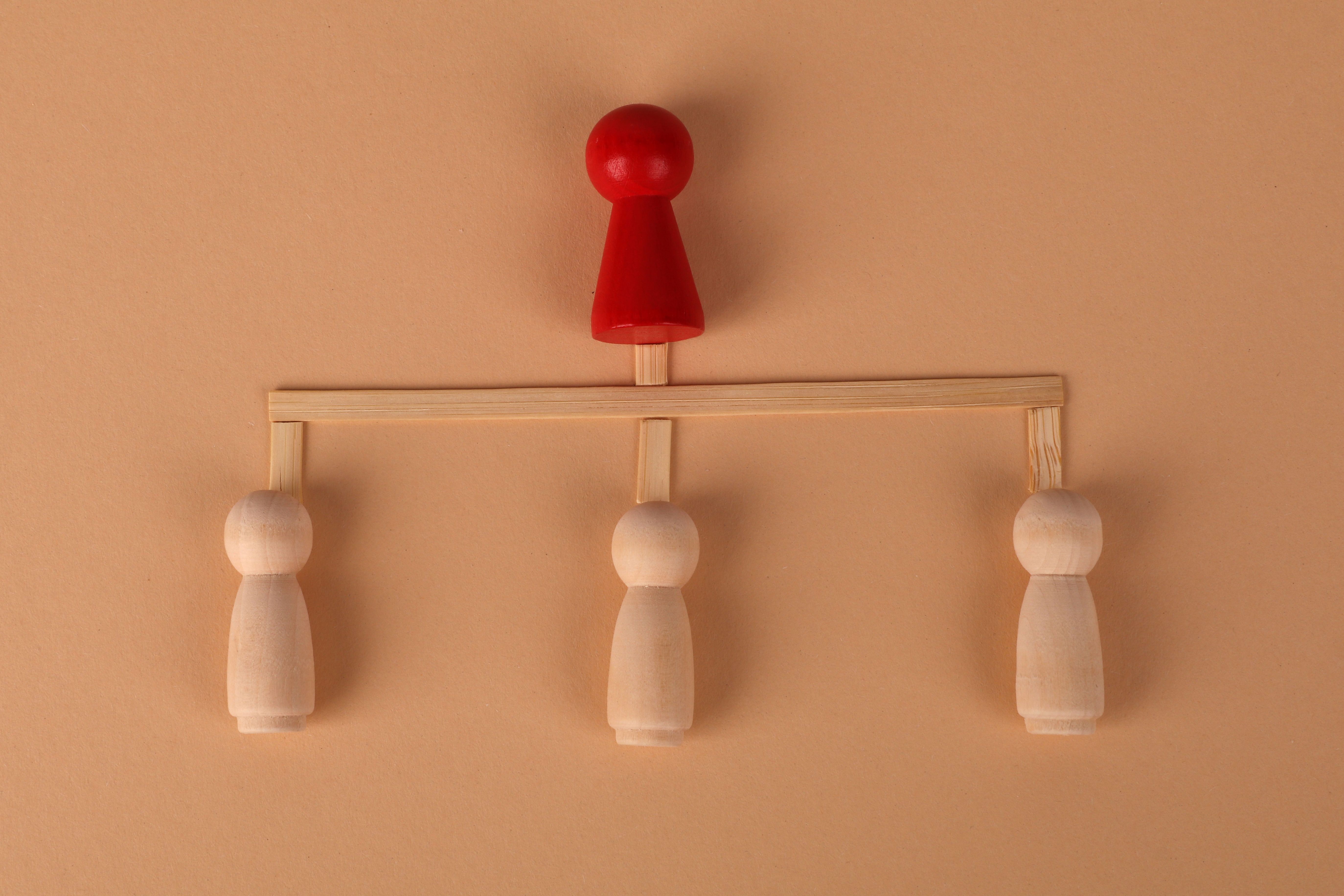 Minimalist arrangement of wooden figures depicting hierarchy and leadership concept.
