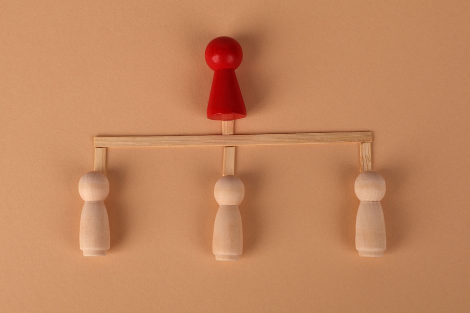 Minimalist arrangement of wooden figures depicting hierarchy and leadership concept.