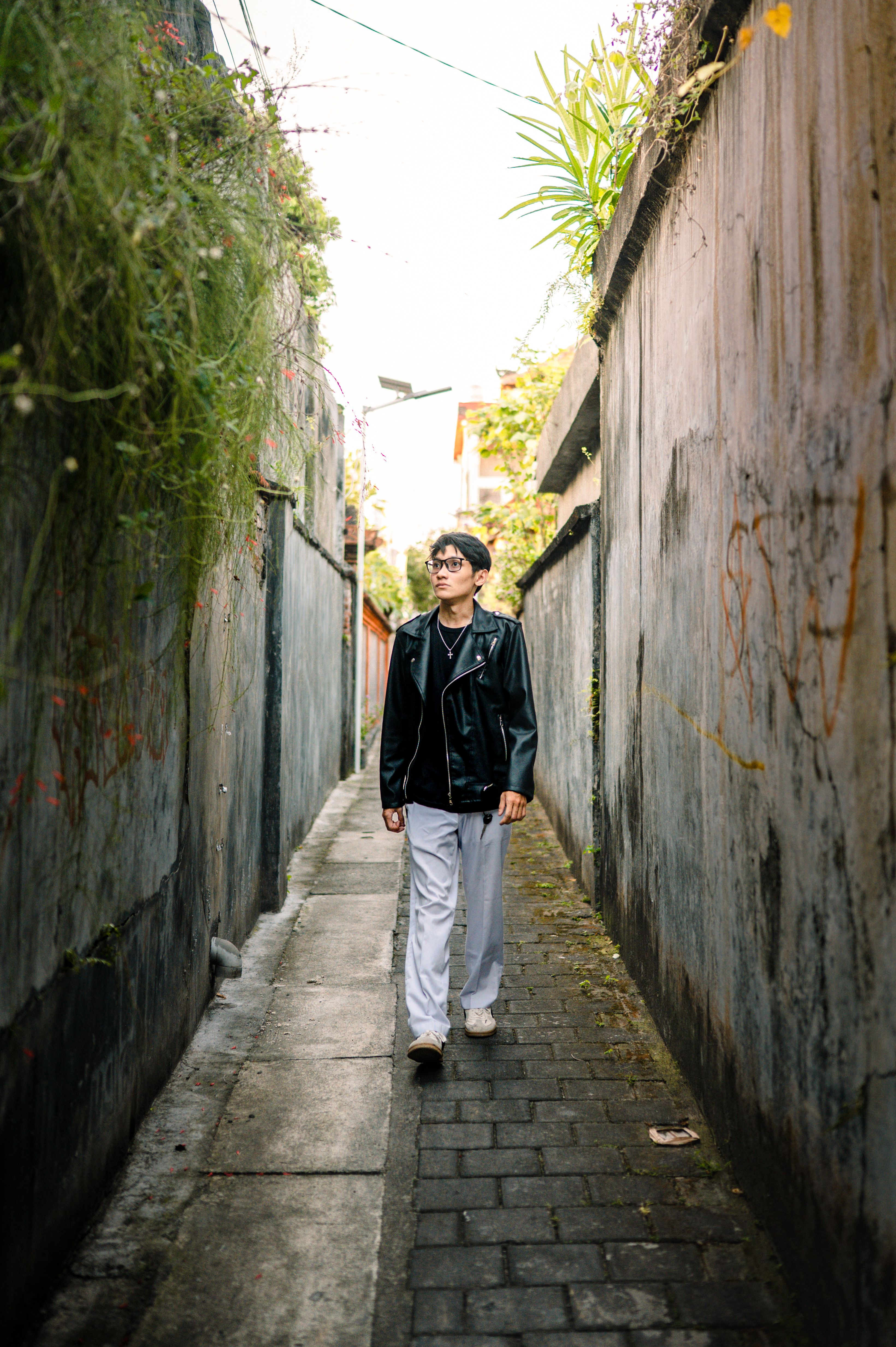 Person walking in a narrow urban alleyway, showcasing a stylish leather jacket look.